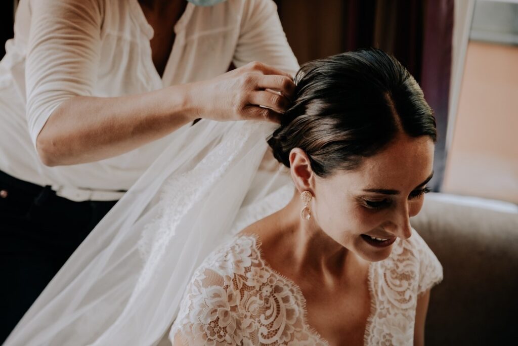 MIO Make-up Artist steckt den Brautschleier in die Haare der fertig gestylten Braut